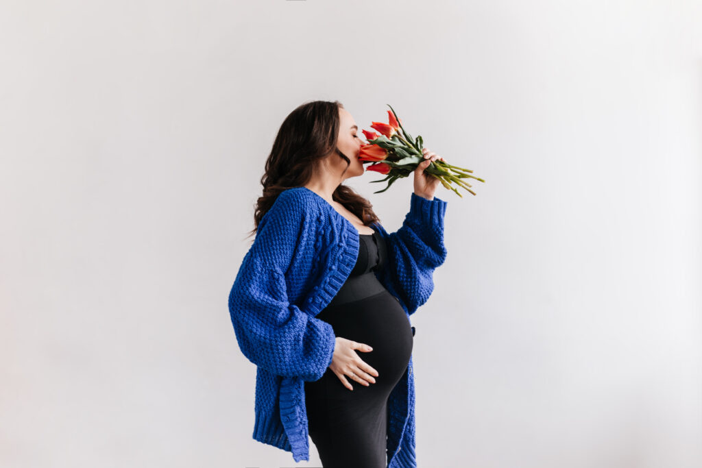 attractive-pregnant-lady wearing maternity clothes smells-tulips-isolated-background